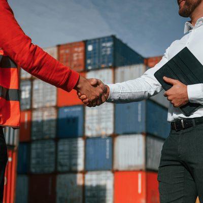 Making handshake. Two male workers is on the location with containers.